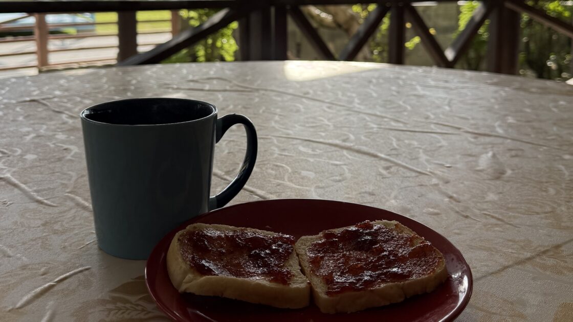 ツバルのフィラモナロッジのテラス席で食べる、マグカップのコーヒーといちごジャムを塗ったトーストの朝食。