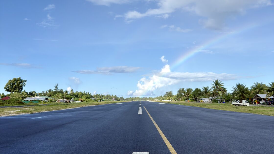 ツバルの雨上がりの滑走路。白線の足元から虹がかかり、背景には青空と雲が広がっている。