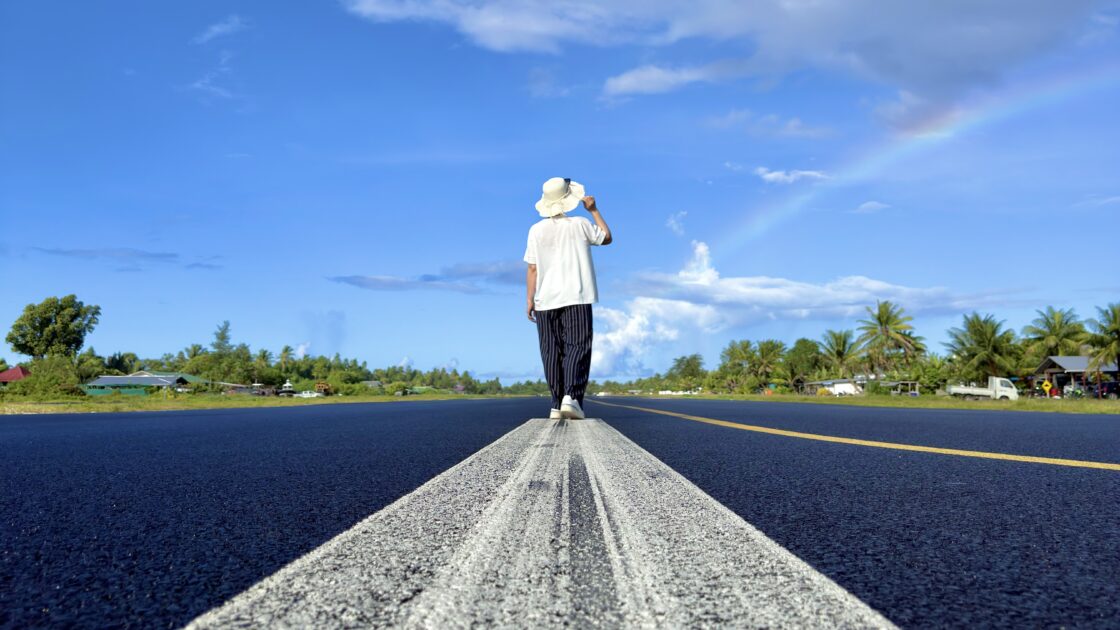 朝のツバルの滑走路の白線の上を歩くはるカタルーニャと、その先にかかる虹