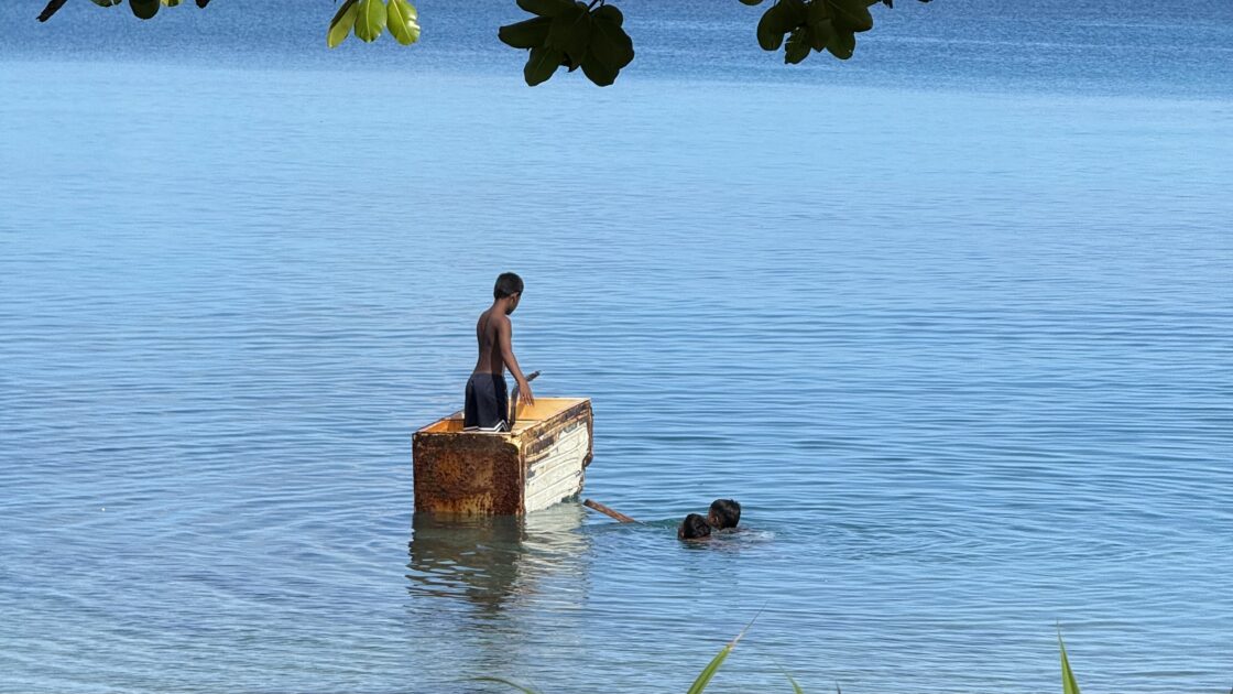 ツバルの海でゴミのコンテナのようなものに乗って泳いだり遊んだりしている子供たち