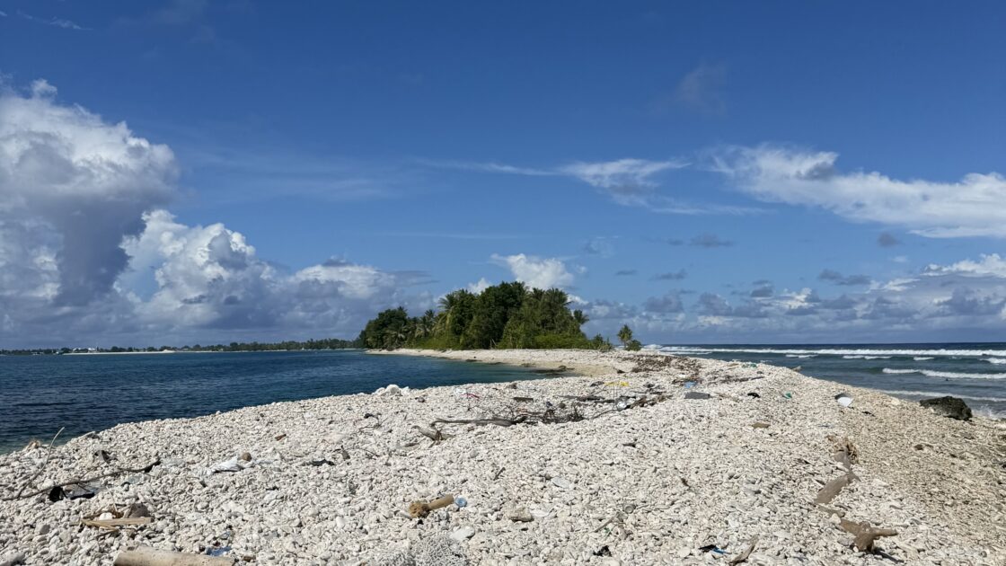 ツバル南端のゴツゴツとした白い石の海岸と、その奥に見える本島の緑、青空、海。