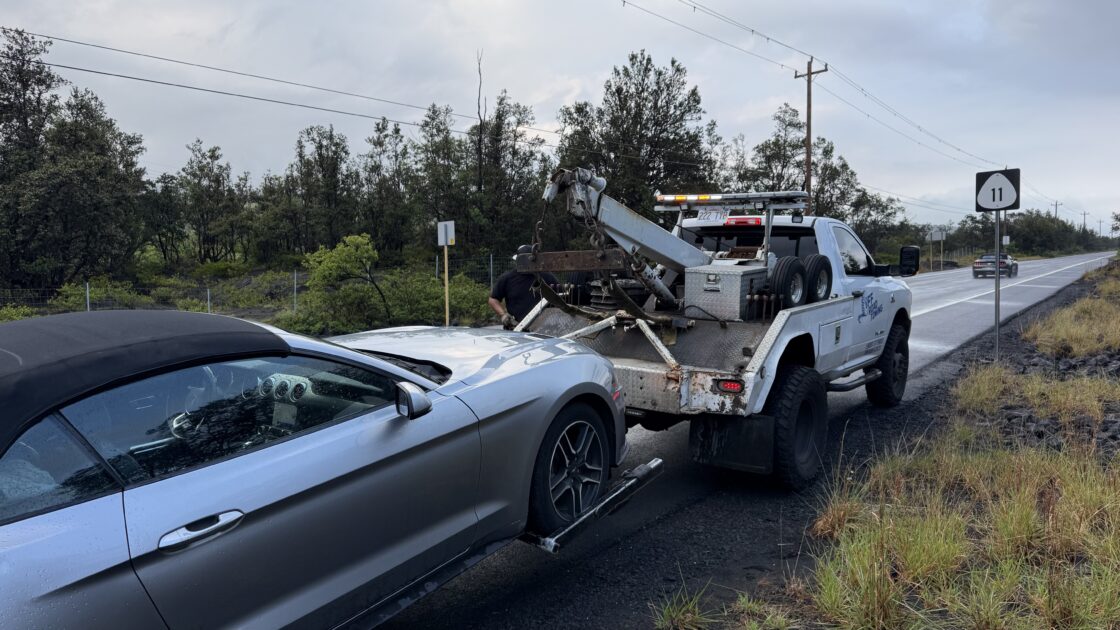 ハワイ島の路肩でレッカー車が銀色のマスタングを牽引フックに接続している様子